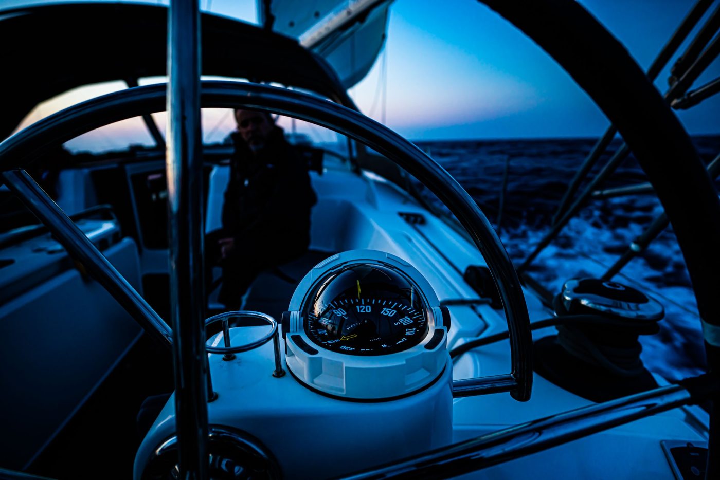 Looking through a sailboat's wheel to the compass and the sea at twilight
