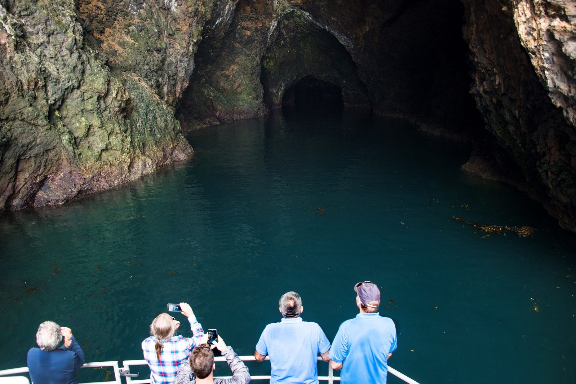 A boatload of visitors approaching the dark entrance of Painted Cave, its walls streaked with color